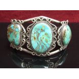 A white metal bangle set with three oval turquoise in scroll mount