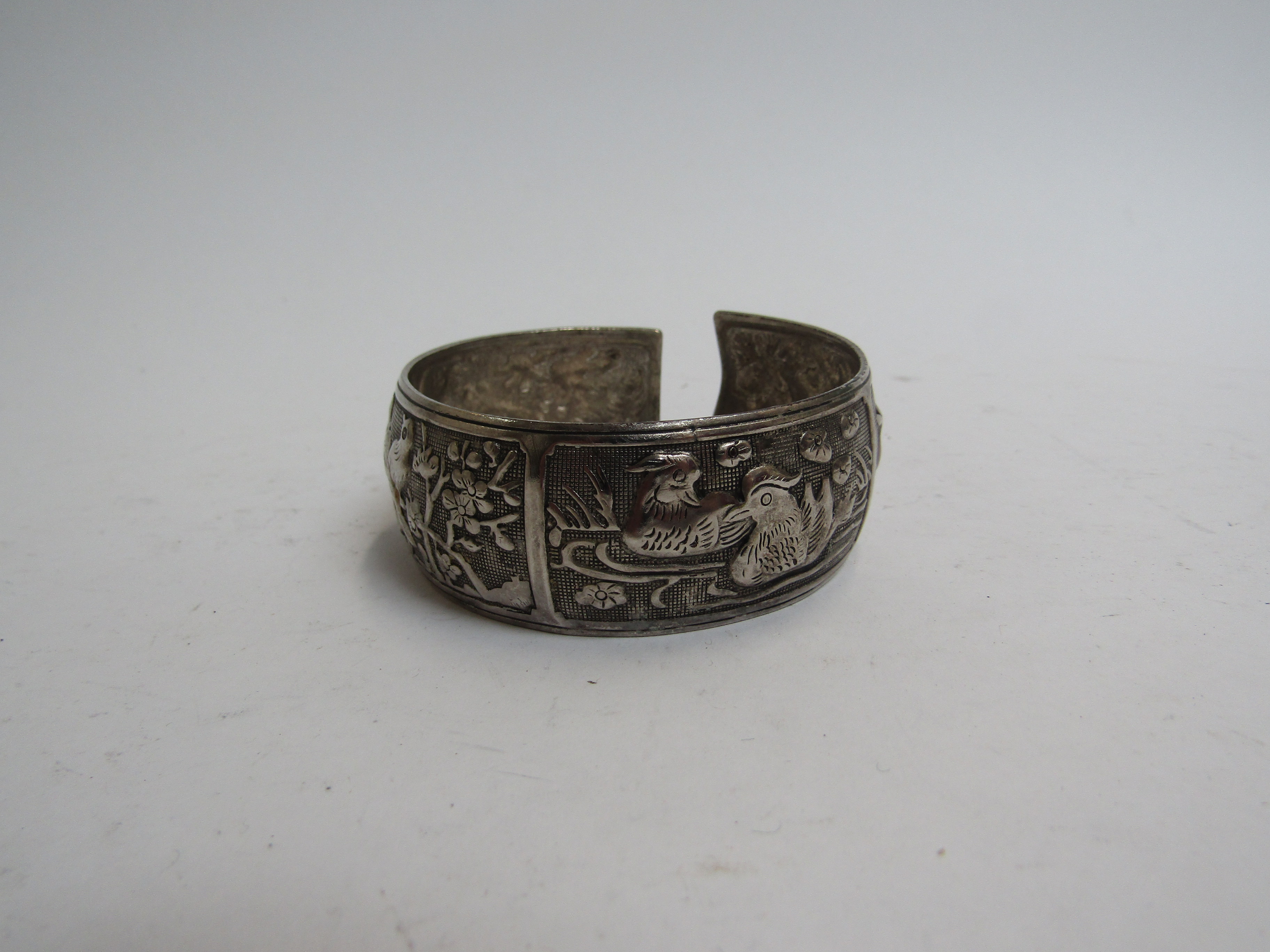 An Eastern embossed silver bangle with panels of birds and wild animals, 6cm diameter,