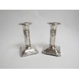 A matched pair of silver candlesticks with square bases and loaded stems, swag decoration,