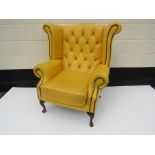 A bright yellow wingback armchair with stud detail, wear present,