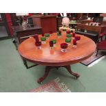 A circular mahogany tilt-top table with turned column, tripod scroll foot legs with ceramic castors,