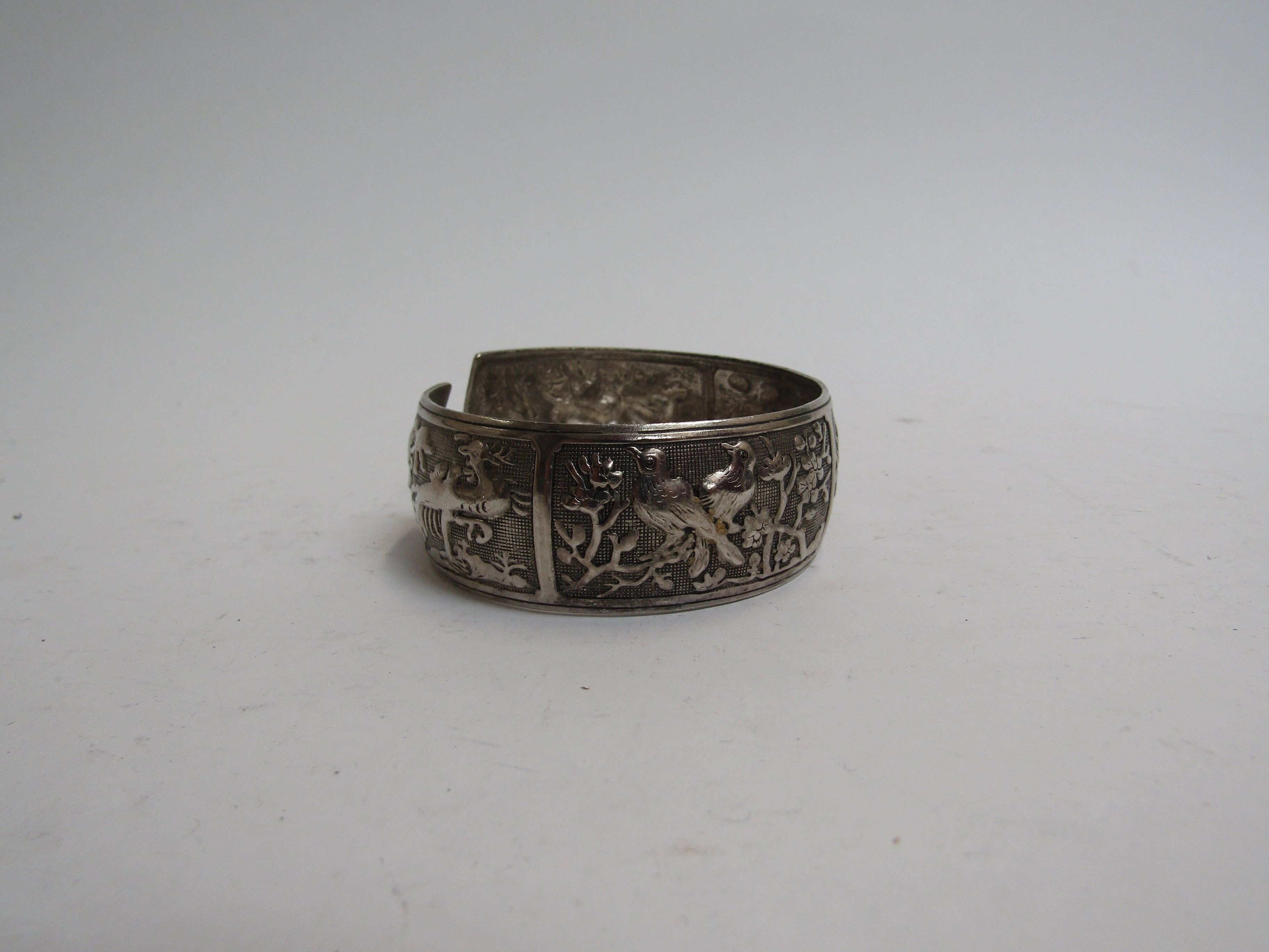 An Eastern embossed silver bangle with panels of birds and wild animals, 6cm diameter, - Image 2 of 2