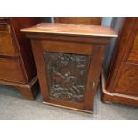 An Edwardian mahogany wall hanging cupboard with carved panel front depicting jockey and horse