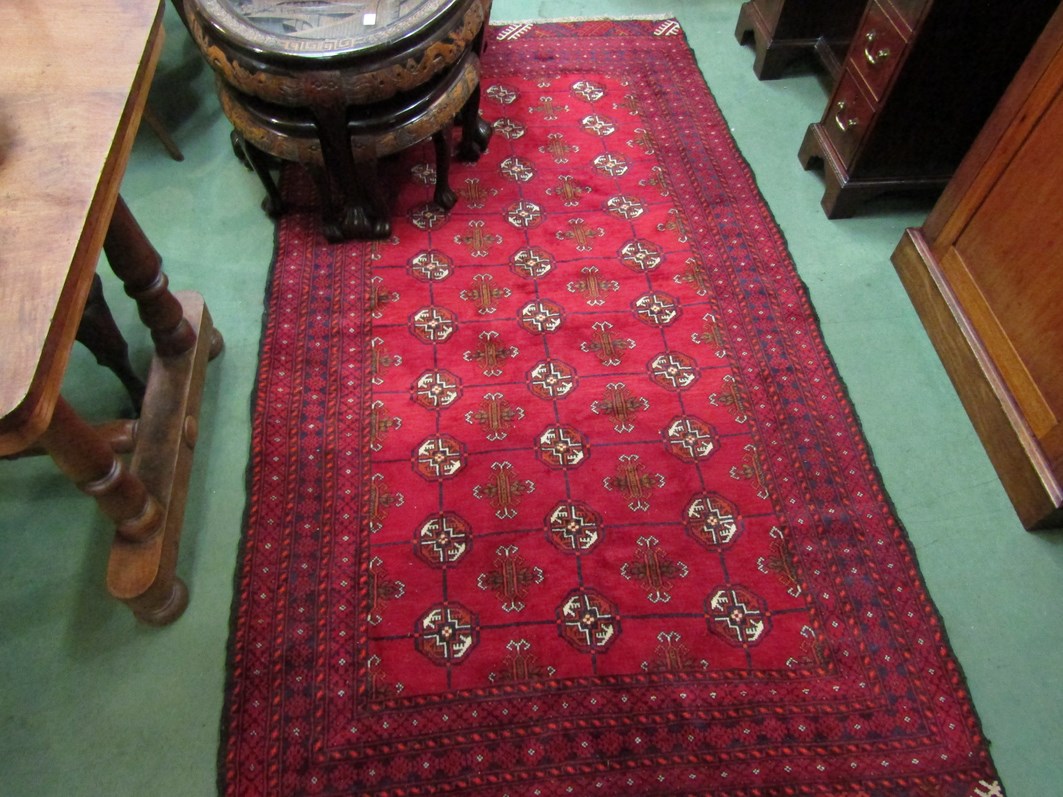 An Eastern red ground wool rug, central field of three rows of guls, multiple geometric borders,