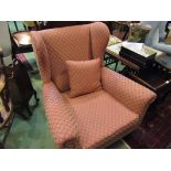 An Edwardian wingback fireside armchair on square tapering legs and castors with scatter cushion