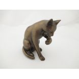 A bronzed figure of a cat licking it's paw,