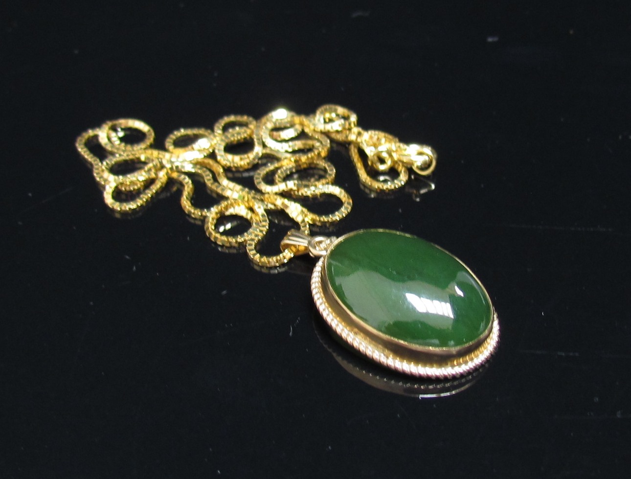 An oval cabochon jade pendant in 10k mount hung on a gold box chain stamped 750, 46cm long, 5.