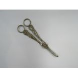 A vintage ornate pair of white metal grape scissors with hunting scene
