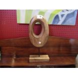 A wooden oval sculpture on stand,