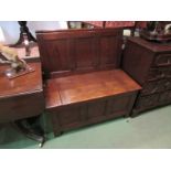 An Arts and Crafts oak box seat settle the panelled back rest over a hinged seat panelled base on