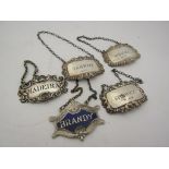 Four various hallmarked silver decanter labels and a silver plate example