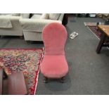 A spoon-back nursing chair with pink upholstery on turned front legs to castors,