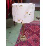 A brass Corinthian form table lamp together with a cream shade decorated with birds