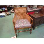 An Edwardian beech bergere armchair the drop in upholstered seat over turned fore legs and