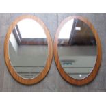 An oval pair of teak backed wall mirrors. Overall 57cm x 36.