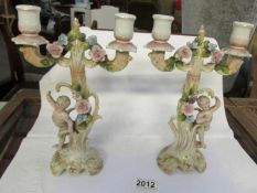 A pair of early 20th century porcelain candlestick surmounted cherubs and with lift off tops.