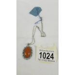 An amber vintage pendant in a pale blue enamel surround with an attached silver chain,