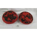 A pair of black and red cinnabar lacquer circular lidded boxes, one decorated with guardian lions,