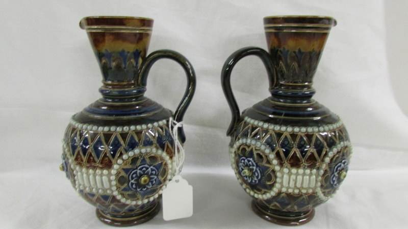 A pair of 16.5 cm Doulton ewers by E Violet Haywood, Minnie Forster and N Taylor.