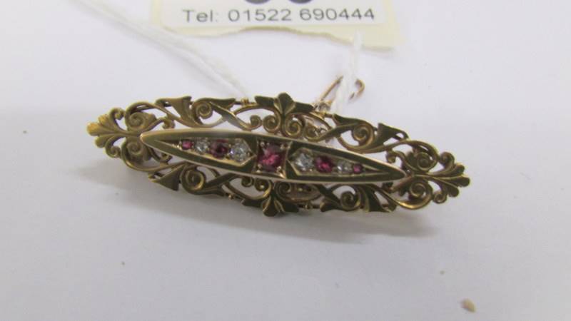 An antique ruby and diamond brooch in 15 carat hall marked gold with attached safety chain.