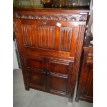 A dark oak drinks cabinet with drop down front and 2 doors with drape carving