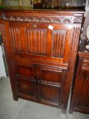 A dark oak drinks cabinet with drop down front and 2 doors with drape carving