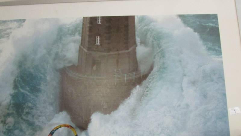 A large framed and glazed print of a lighthouse in rough seas.