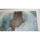 A large framed and glazed print of a lighthouse in rough seas.