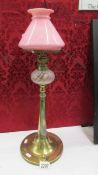 An arts and crafts oil lamp on brass base with glass font and pink glass shade (no chimney).