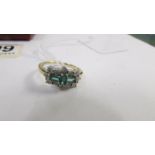 A yellow gold ring set with three oblong emeralds surrounded by diamonds. Size N.