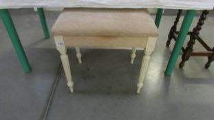 A painted bedroom stool on reeded legs with cream fabric covering.