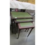 A nest of 3 dark wood stained tables with green leather insets.