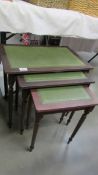 A nest of 3 dark wood stained tables with green leather insets.