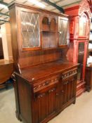 A dark oak cottage dresser with leaded glass doors and drape carved panels,