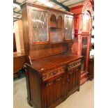 A dark oak cottage dresser with leaded glass doors and drape carved panels,