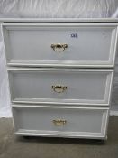 A white 3 drawer bedroom cabinet on casters.