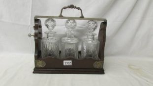 A 3 bottle Tantalus complete with 3 cut glass bottles and key, in good condition.