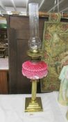 A Victorian brass oil lamp with reeded column, pink glass font and complete with burner and chimney.