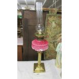 A Victorian brass oil lamp with reeded column, pink glass font and complete with burner and chimney.