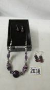 A purple glass costume necklace with matching earrings and another pair of earrings.