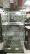 A glass display case - 'Rolex', 'Breiling', 'Omega'.