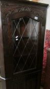 A dark oak corner cabinet with linen fold bottom door and leaded top door.