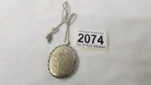 A silver locket with textured front engraved with a flower, all silver.