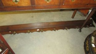 A long oak coat rack with brass 'Cherub' hooks.