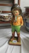A painted plaster? model of a boy in waders and a fishing hat smoking a pipe on a square base with