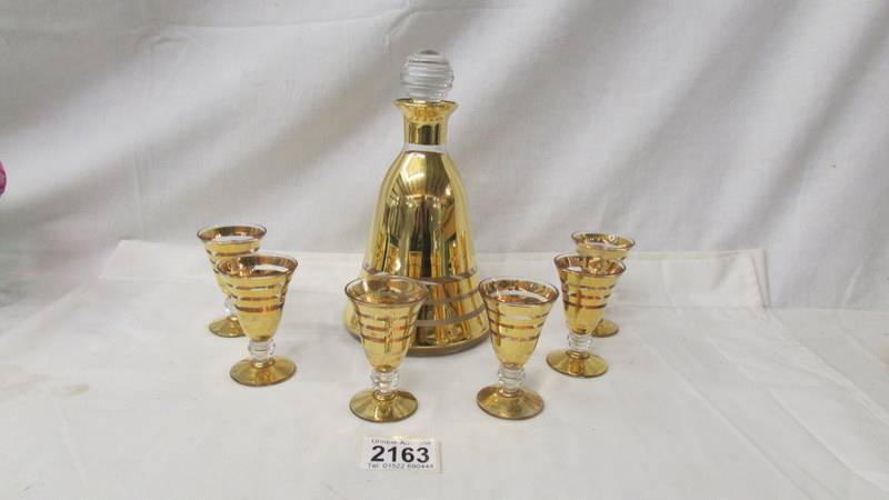 A mid 20th century gilded liquor decanter with 6 matching glasses.
