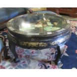 A circular Chinese lacquered table with applied figures under glass top (collect only).