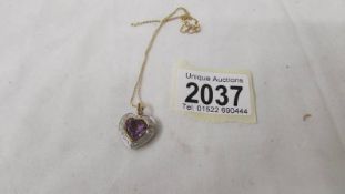 A heart shaped gold locket with central amethyst surrounded by diamonds.