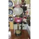 A Victorian brass Corinthian column oil lamp with cranberry glass font and alter shade,