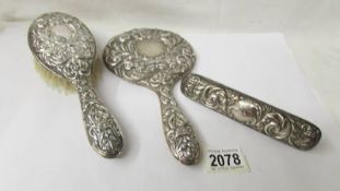 A silver backed hand mirror and two silver backed brushes, (one brush a/f).